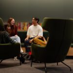 Group of students sitting in front of some books, talking.