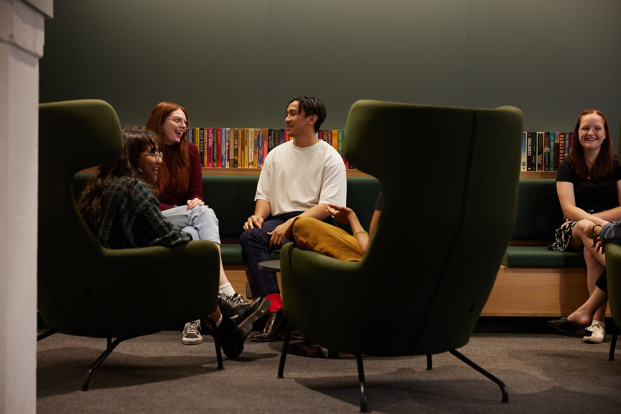 Group of students sitting in front of some books, talking.